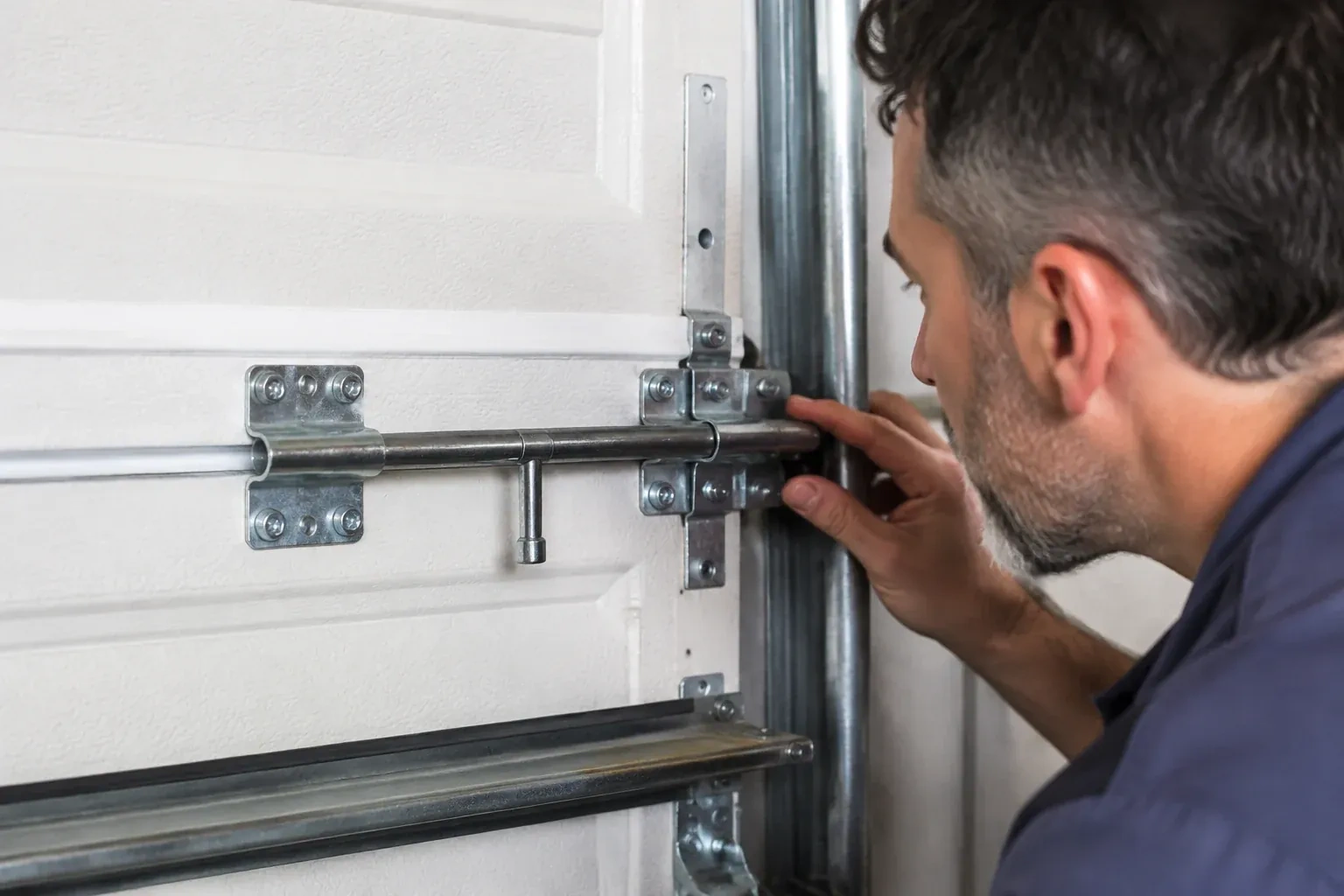 Person leaning close to a white paneled door, one hand on a metal slide-bolt bar mounted across the panel. — Garage Door Manual Lock Repair, Haldimand County
